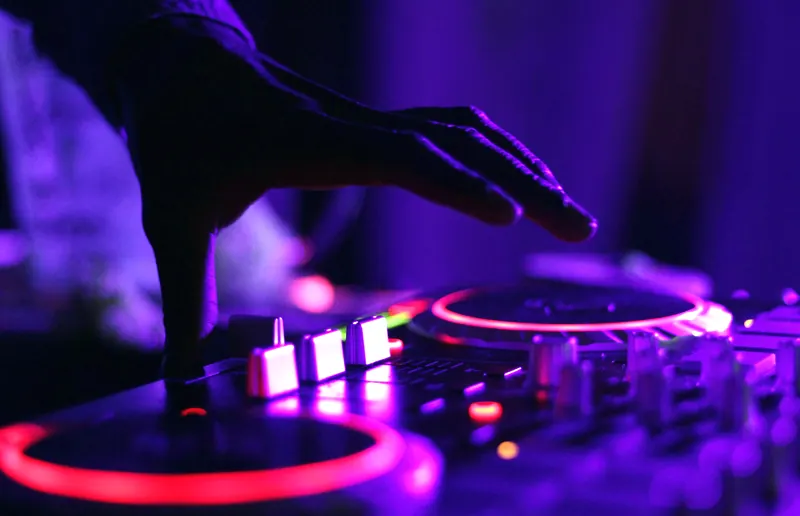 DJ-Pult mit Händen am Mischpult im violetten Licht